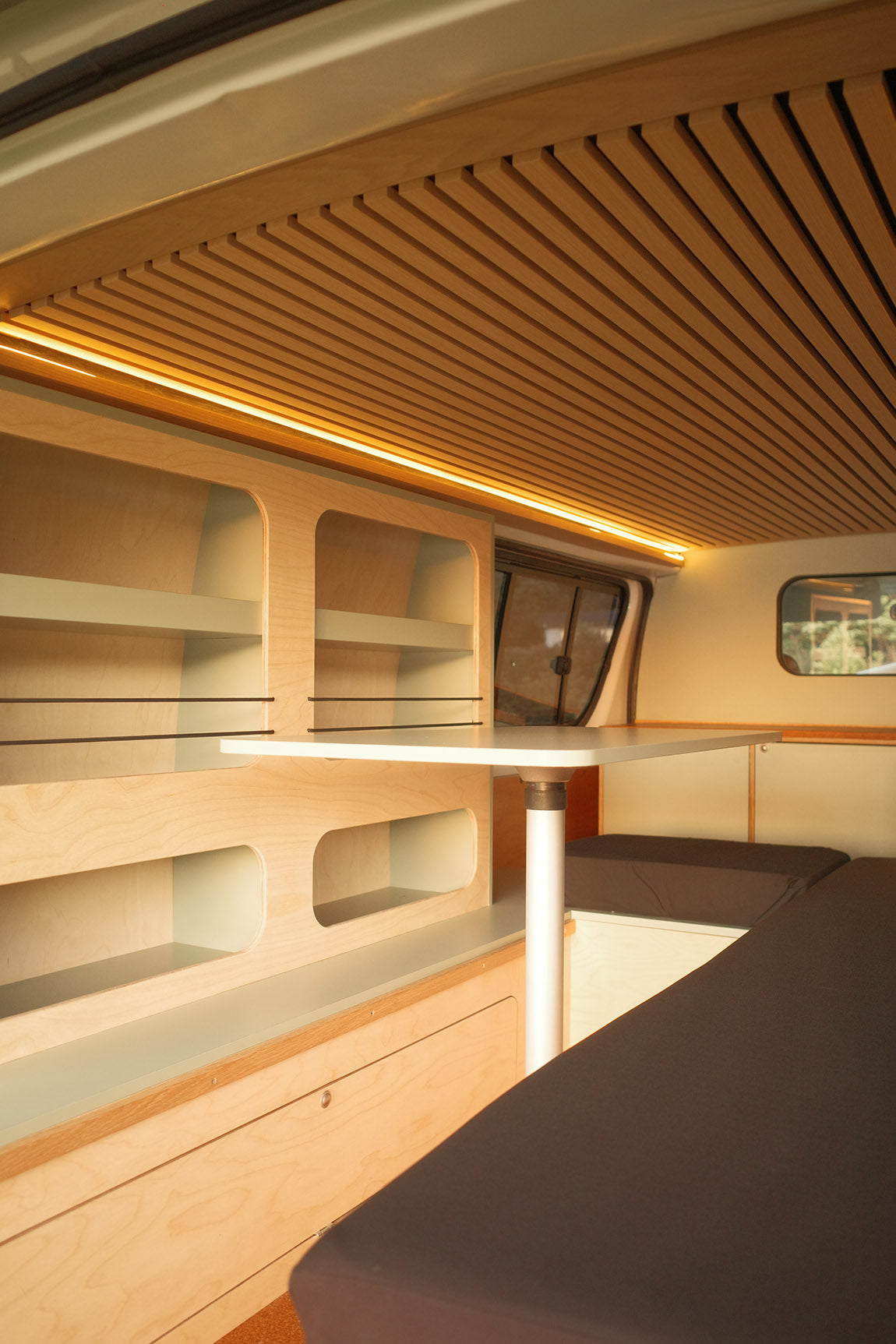 Modern minimalist campervan conversion interior with wooden paneling, shelves, and a small table.