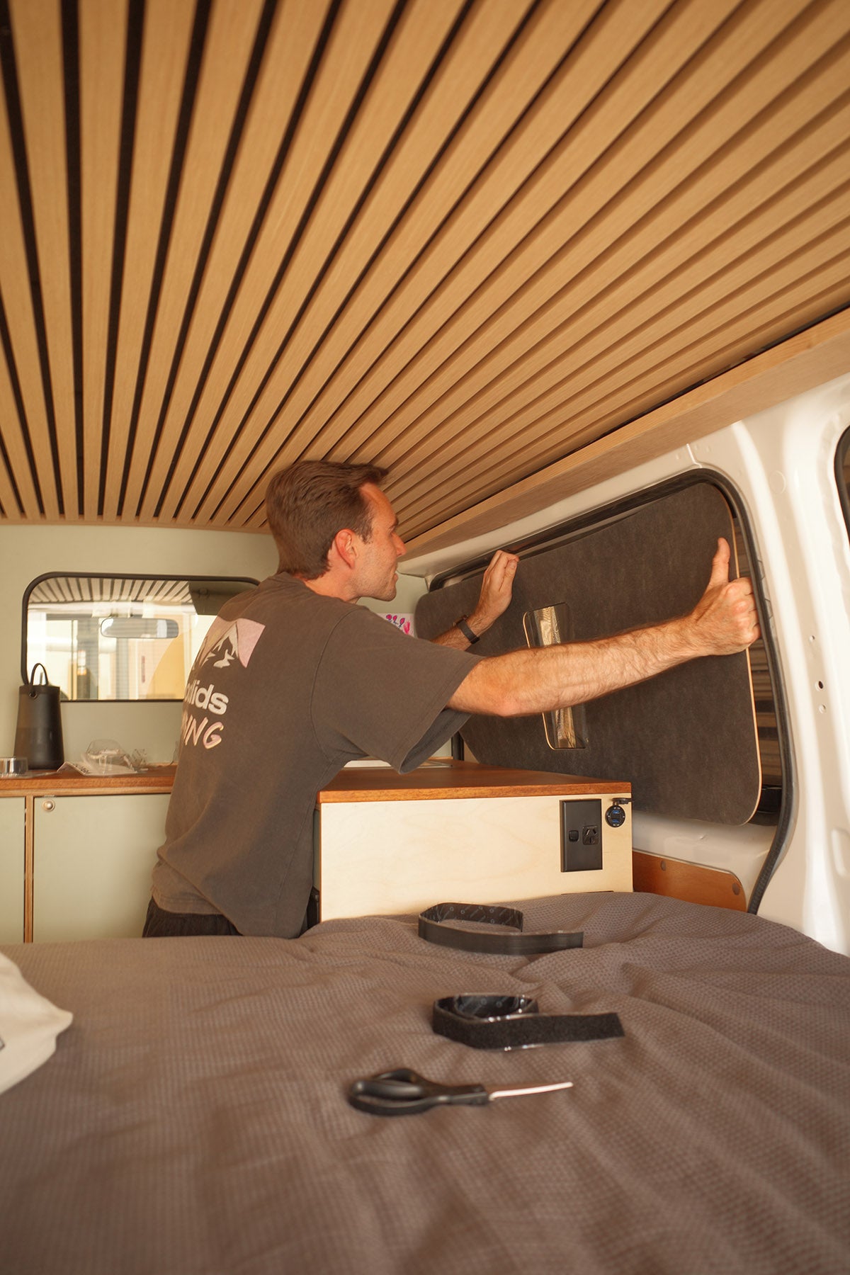Cam working on a van camper conversion interior with wooden paneling.